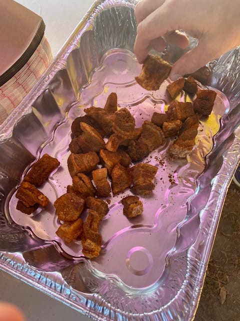 A foil serving tray contains chunks of deep-fried and heavily-seasoned pork belly.